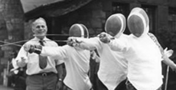 An old black and white photograph shows an instructor teaching three visually impaired fencers in full gear how to fence.