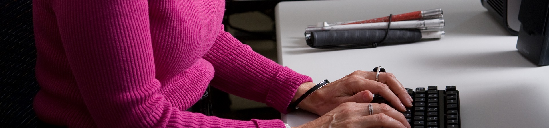 With her white cane folded on the desk, a visually impaired woman types on a computer at the Carroll Center for the Blind.