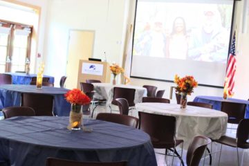 Several round tables are set up in the Technology Center's massive auditorium. A podium and projector screen are in the background.