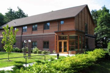 A view across the green grass of the Rachel Rosenbaum Technology Center, a large brown modern building that houses both the technology program as well as dormitories.