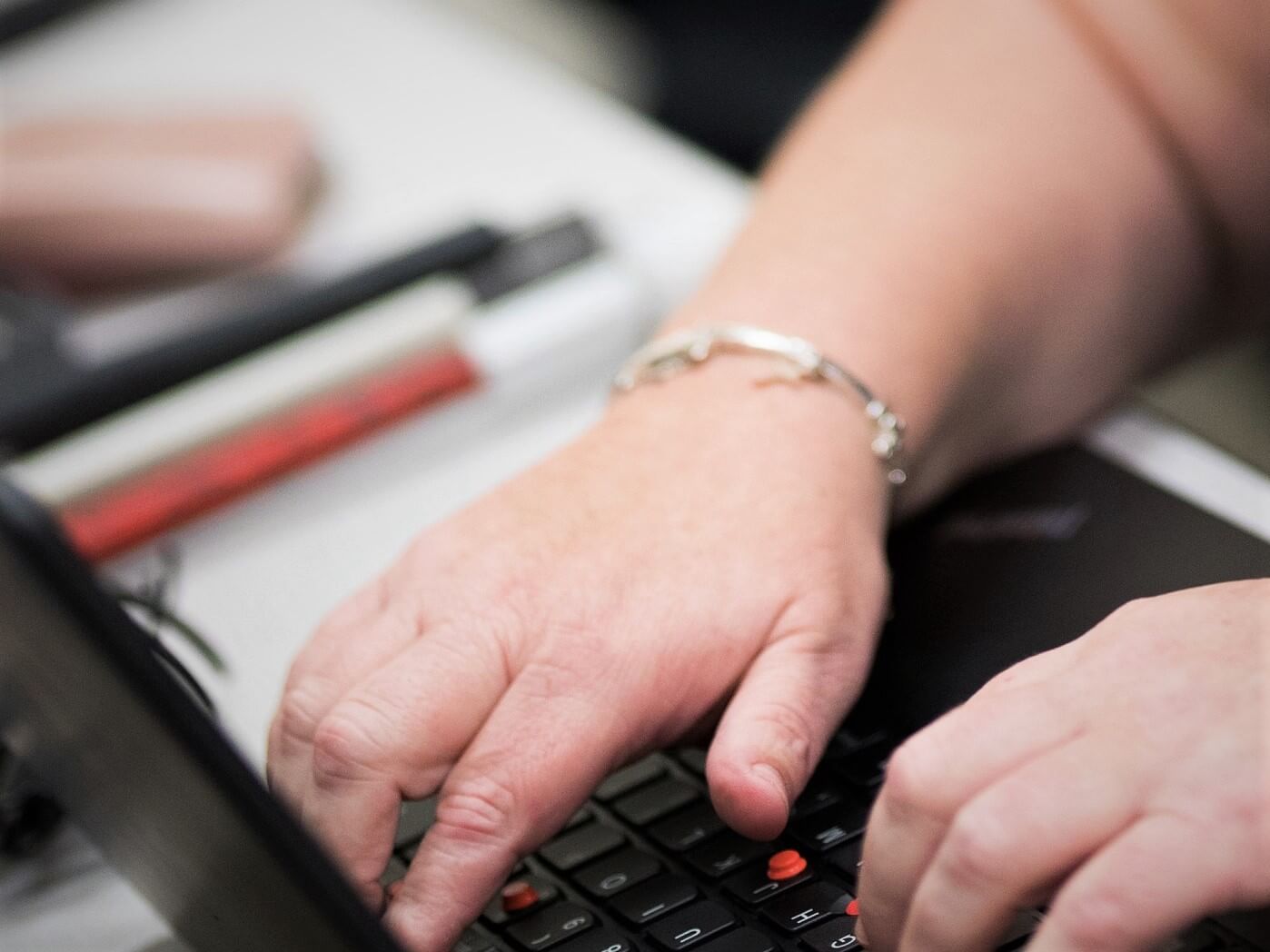 A woman uses a laptop to access a digital document. Her white cane is folded up on the desk next to the laptop.