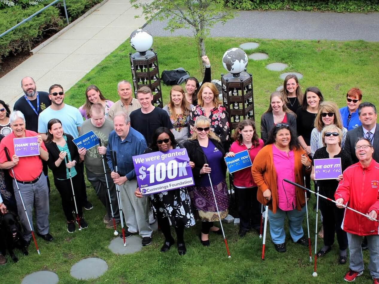 A group of 28 Carroll Center clients and staff hold up various “Thank You” signage at the Carroll Center for the Blind campus in Newton, MA.