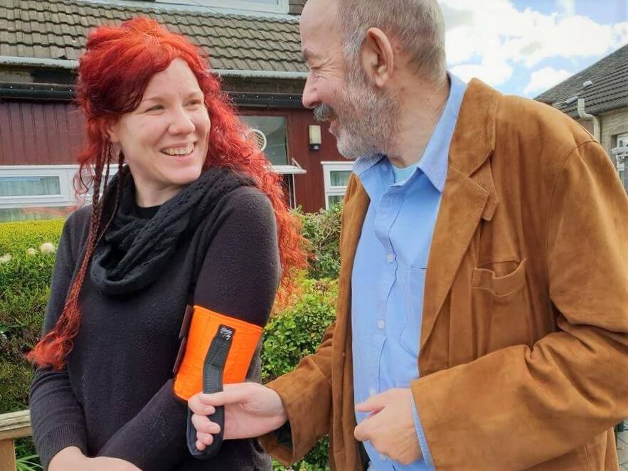 Ramble Tag founders Laura Maclean and Tom Forsyth look at each other and laugh while demonstrating how to use an orange Ramble Tag guidance aid.