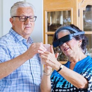 A woman wearing an assistive technology headset shows a man something on her phone.