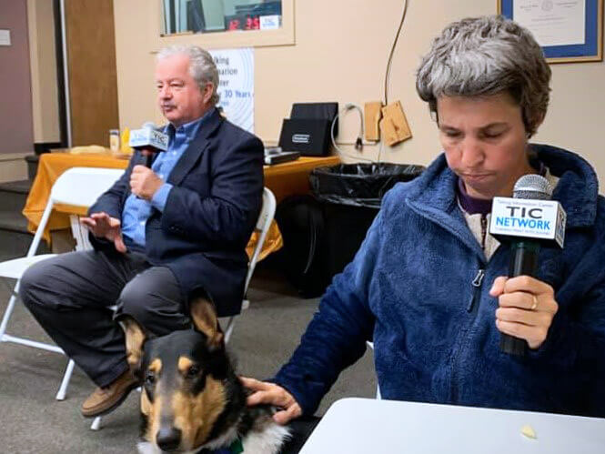 Bob McGillivray and Kerry MacDonald, sit in front of an audience at a South Shore Collaborative Low Vision Support Group session. They each hold microphones with the TIC Network logo on them.