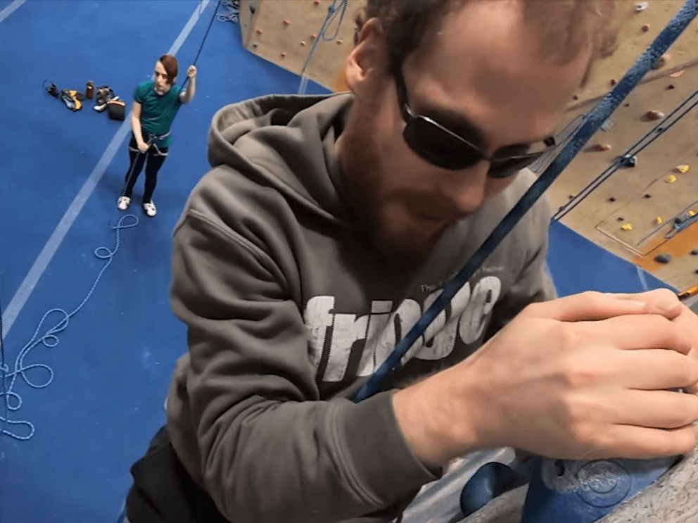 An aerial view from above Matthew Shifrin as he scales a rock climbing wall at an indoor climbing gym.