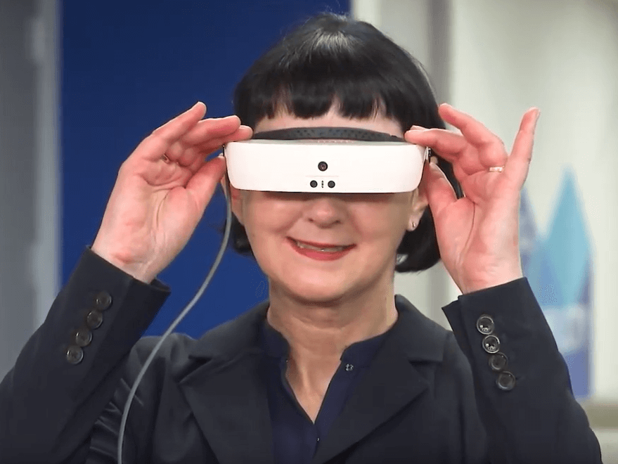 A woman smiles as she puts on a pair of white eSight glasses.