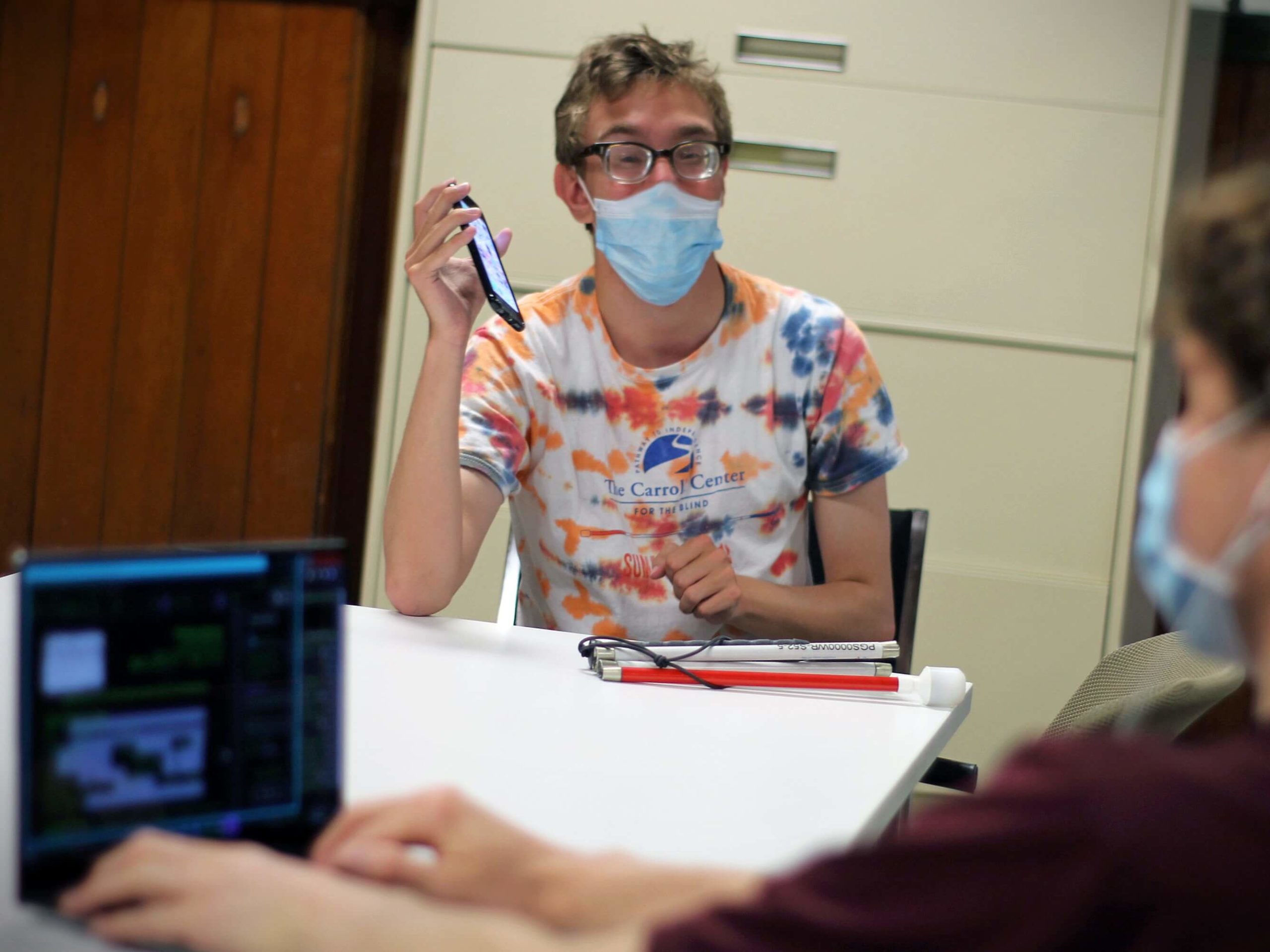 During a technology instruction lesson, a youth summer program student wearing a face covering works on his smartphone.