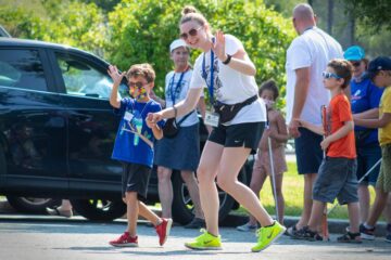 An instructor and Carroll Kids student hold hands and wave at the camera as they walk across a parking lot.