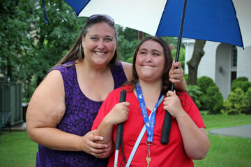 During move-in day at the Carroll Center for the Blind, a smiling mother and daughter pose under an umbrella as they say goodbye to each other.