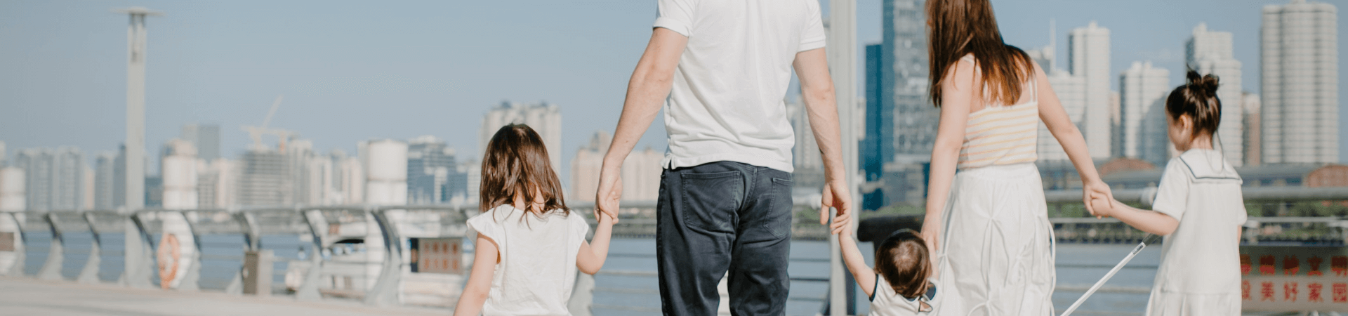 A mother and father hold hands with their three daughters as they walk along a boardwalk.