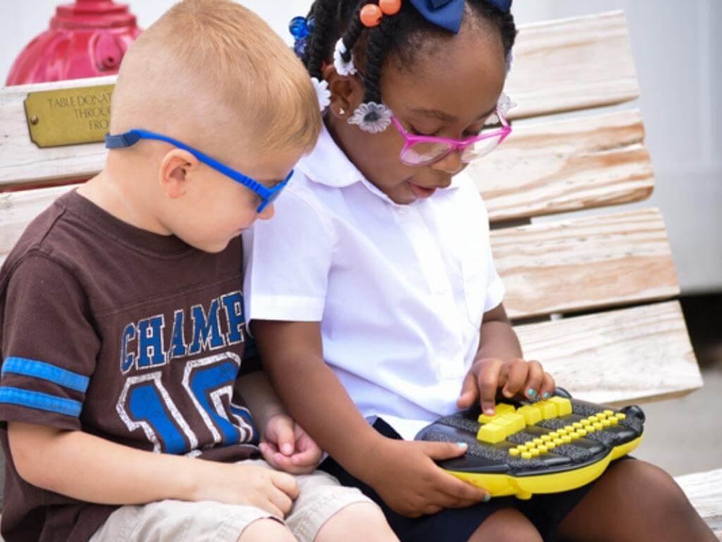 Two children sitting on a bench with a Braille Buzz in their laps.