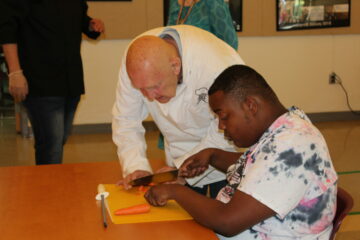 Chef Joe showing cat's paw technique to a Carroll Center student at the cooking demonstration class