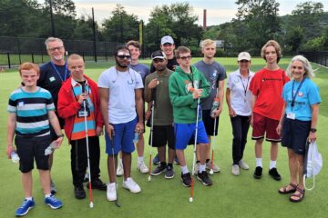A large group of Carroll Center students, instructors, and USBGA coaches smiling for a group photo at the golf course