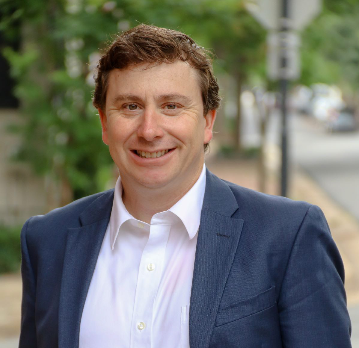 A headshot of Billy Parker, a white man with short blond hair, wearing a white shirt and a blue blazer