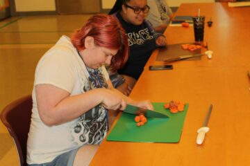 A girl smiling while cutting a carrot at the cooking demonstration class