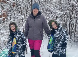 Twin boys, Jason and Daniel, laughing in the snow with their mom, Elizabeth