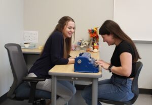 Teacher of Students with Visual Impairments instructing a student how to use a brailler at school