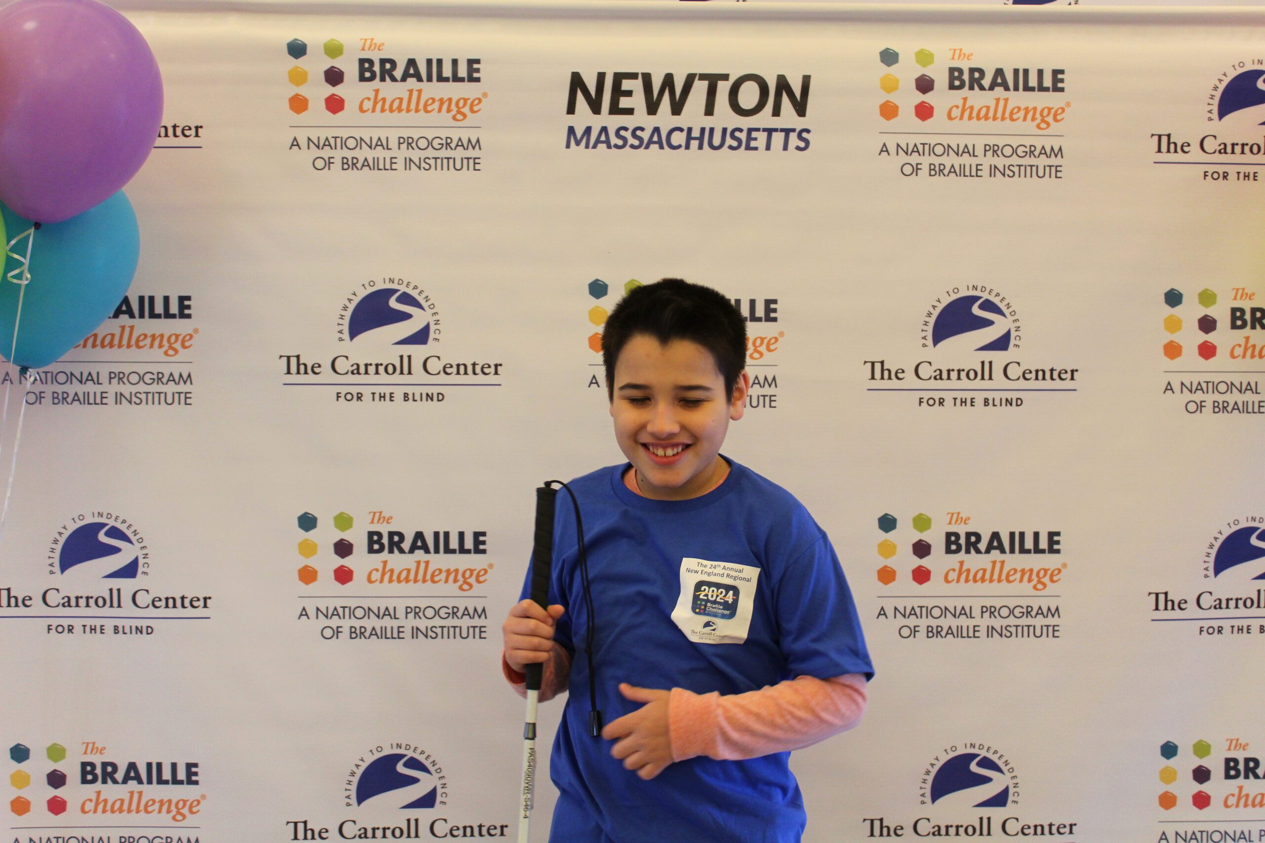 Braille Challenge participant smiling for a photo in front of the Carroll Center Braille Challenge backdrop