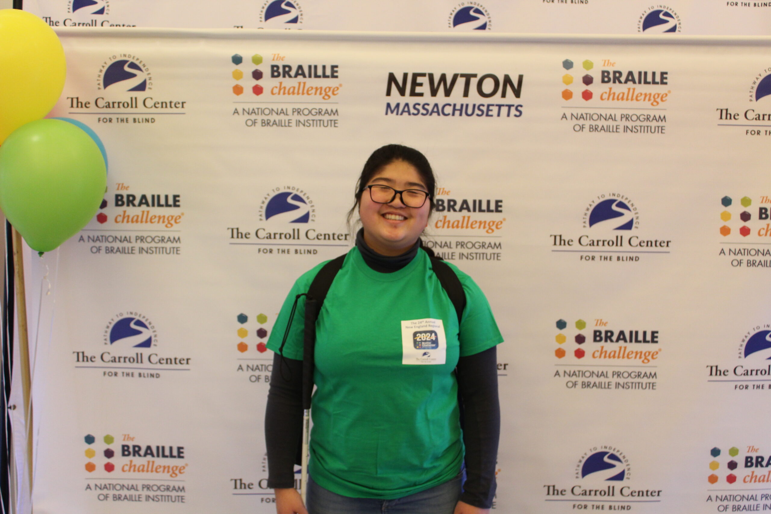 Braille Challenge participant smiling for a photo in front of the Carroll Center Braille Challenge backdrop