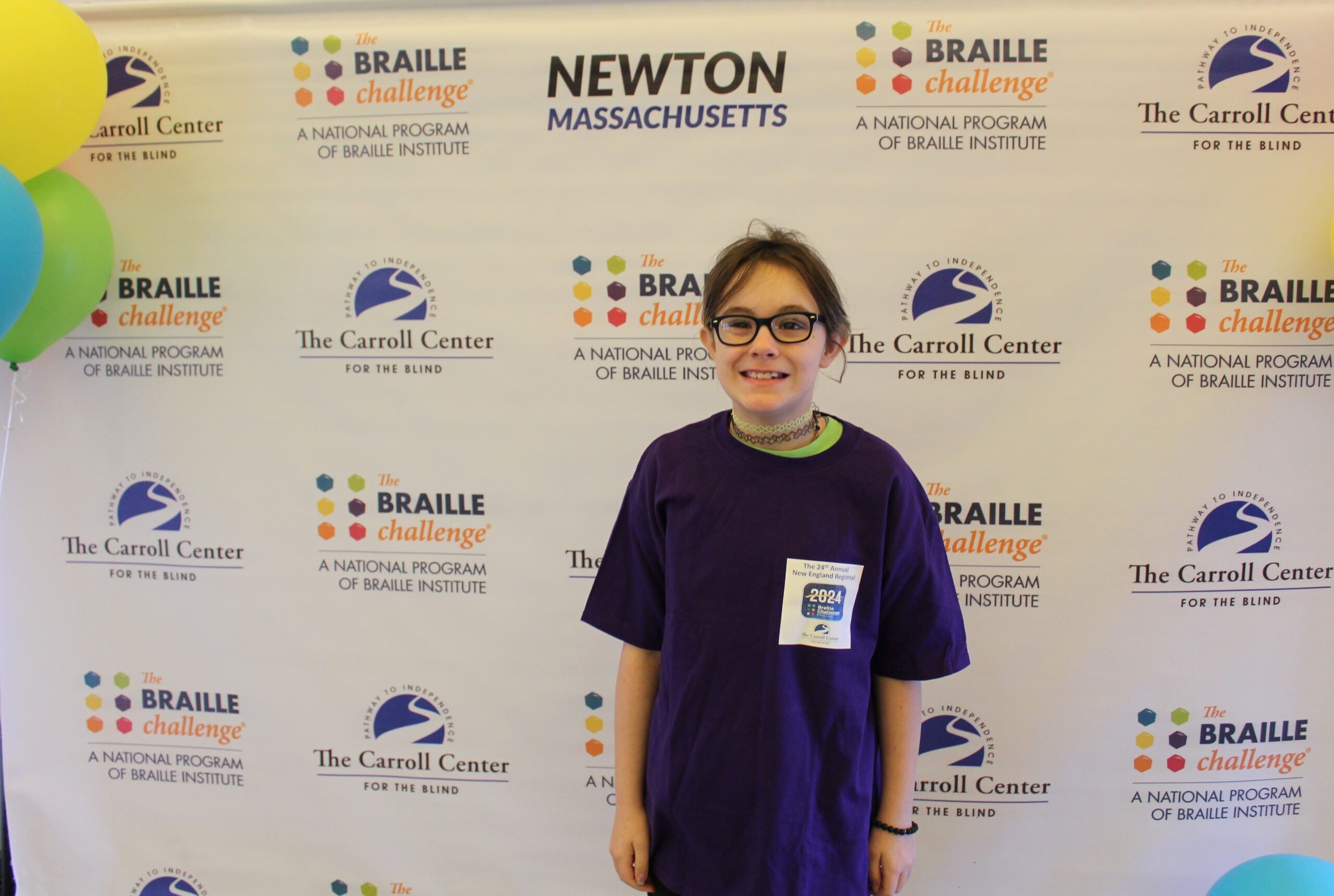 Braille Challenge participant smiling for a photo in front of the Carroll Center Braille Challenge backdrop