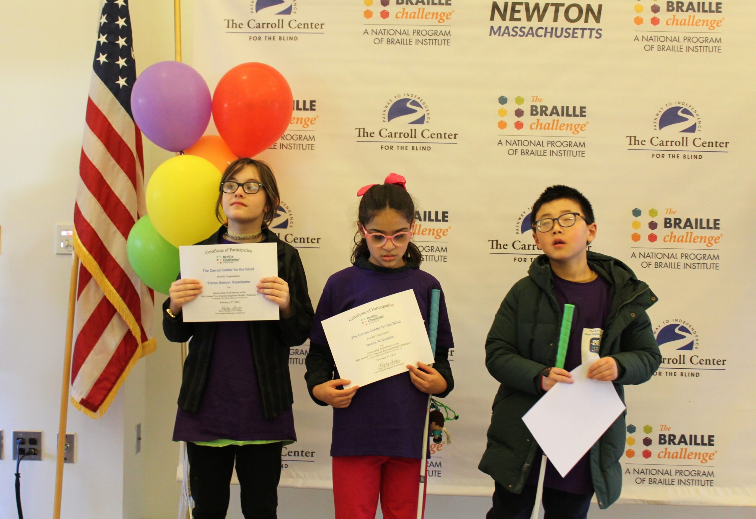 3 Braille Challenge participants smiling for a photo with certificates in front of the Carroll Center Braille Challenge backdrop