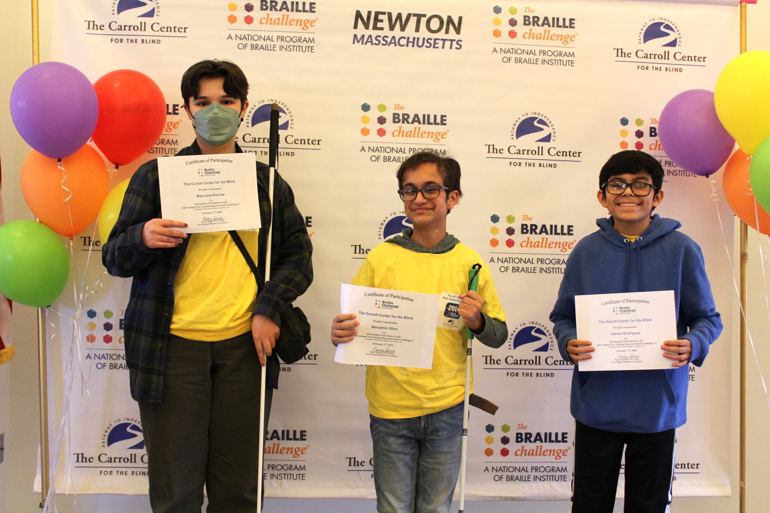 3 Braille Challenge participants smiling for a photo with certificates in front of the Carroll Center Braille Challenge backdrop
