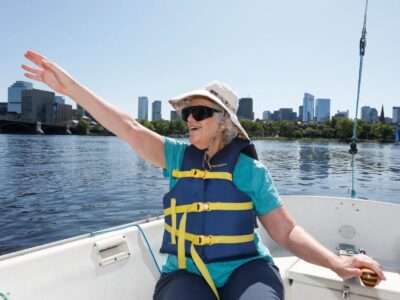 An older blind woman smiles as she steers a sailboat.