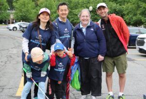 4 adults and 2 young boys, one of whom is holding a white cane, are standing outside and smiling for a group photo. They are wearing Carroll Center for the Blind Walk for Independence T-shirts.